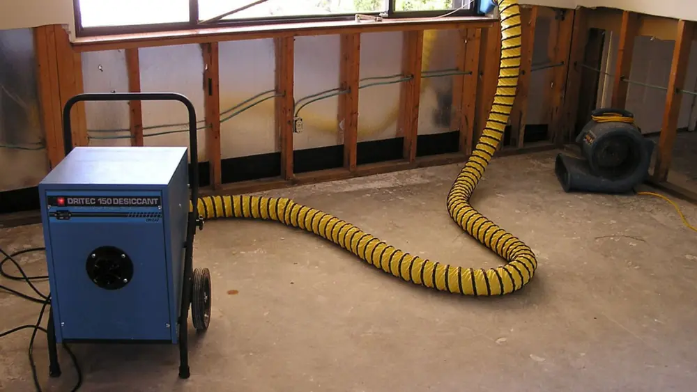 Dehumidifier with a yellow duct hose beside opened wall framing